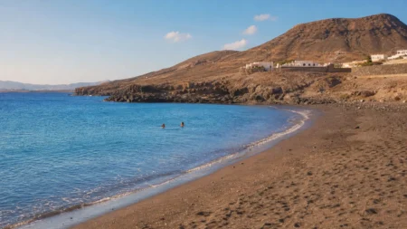 Petite plage volcanique du sud de Tenerife en fin d'après-midi, mer calme et collines arides